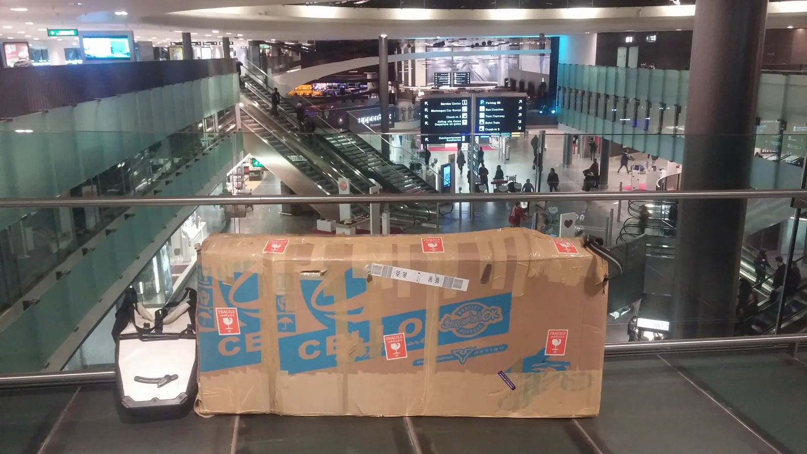 蘇黎世機場航廈內一個貼滿易碎標籤的紙製單車箱，旁邊放著隨身行李
