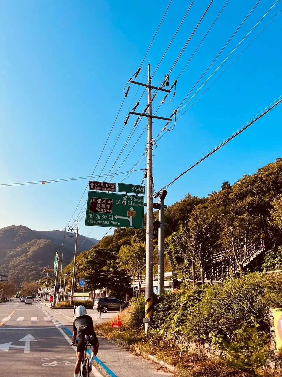 路口綠色路牌指向花開市場與雙磎寺,下方有選手騎車經過