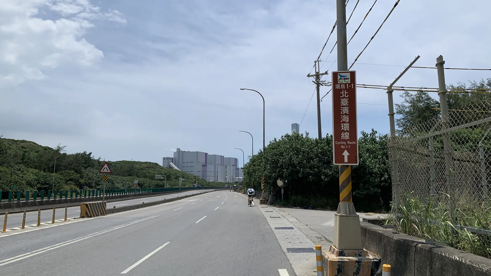 濱海公路旁的「環島1-1 北臺濱海環線」棕色指標，遠處有一位騎士