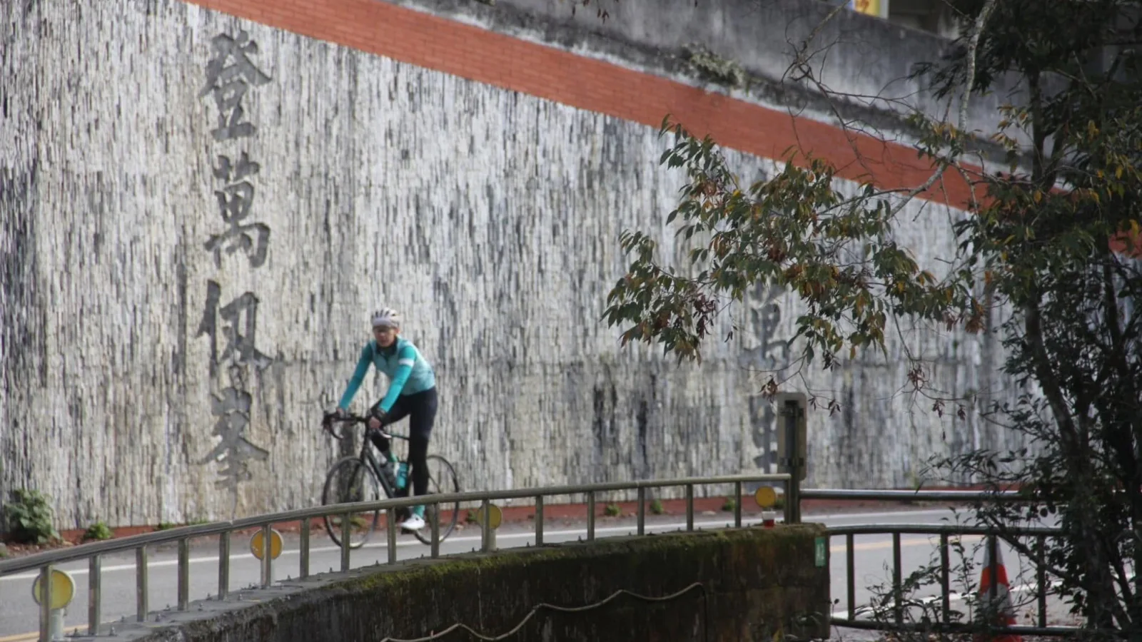 公路車騎士通過中橫公路沿線的橋段,背景是刻字的擋土牆