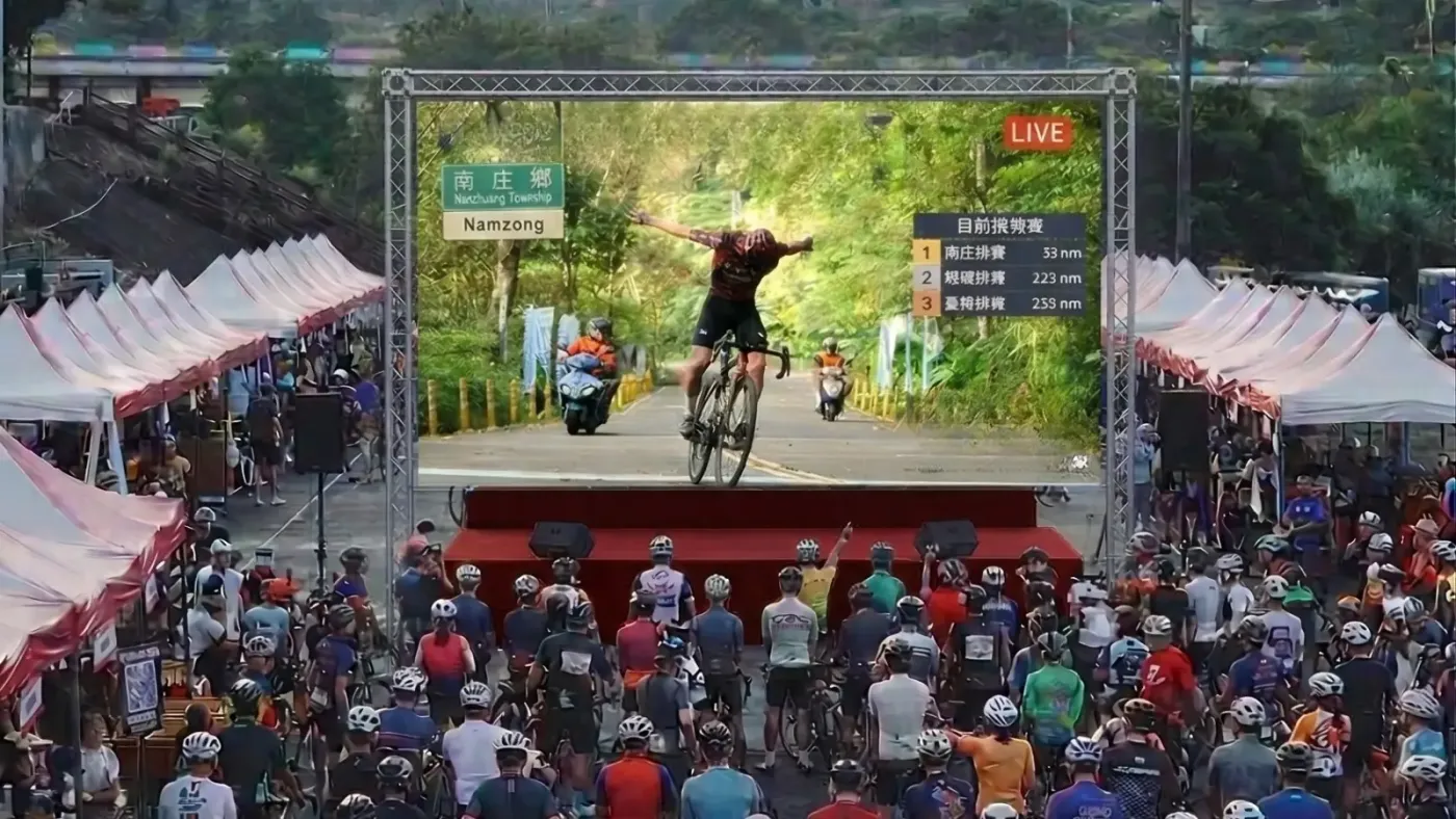 會場大螢幕直播選手在南庄鄉界舉手衝線，觀眾在螢幕前圍觀