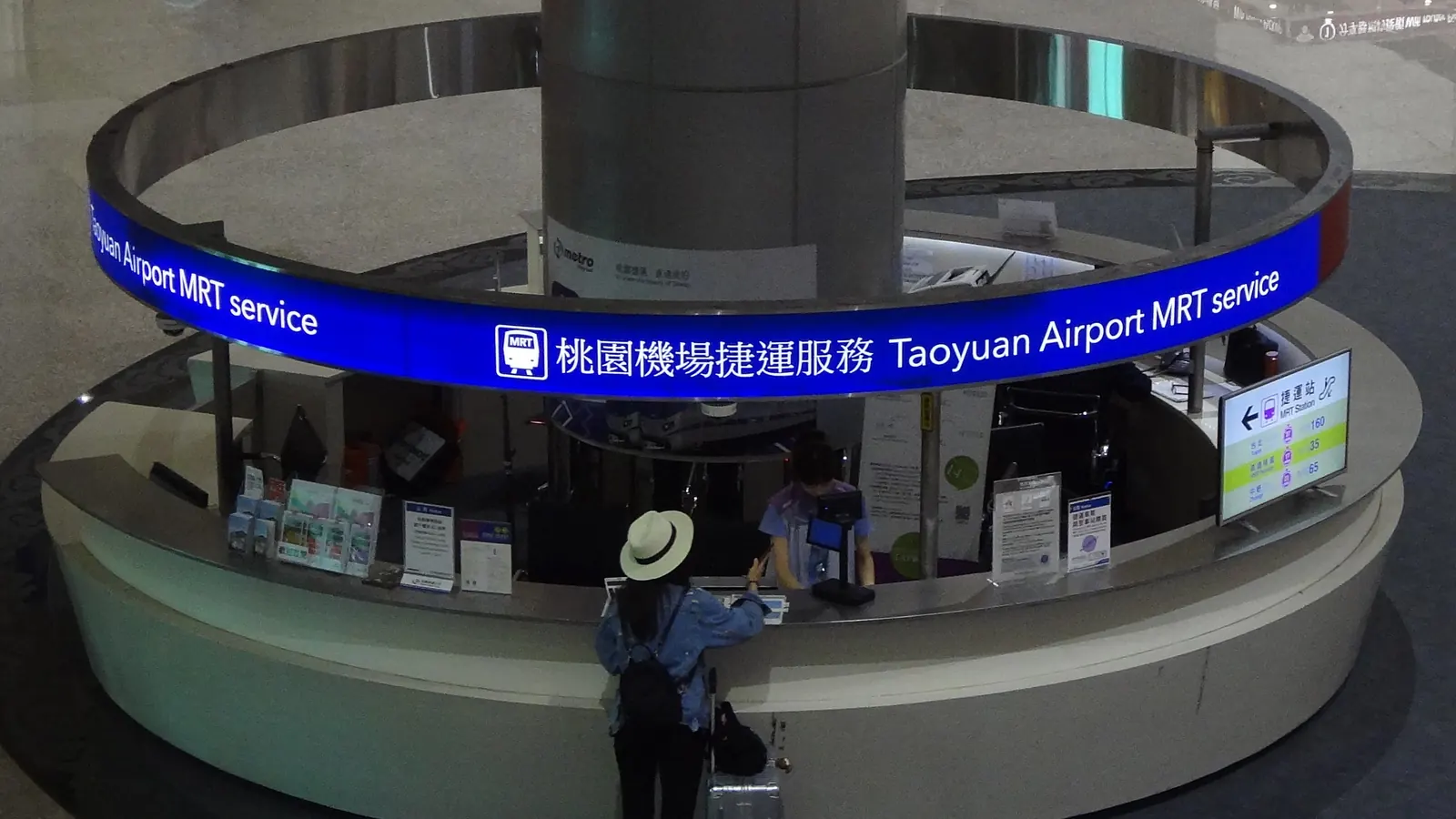 第二航廈內的圓形「桃園機場捷運服務」諮詢櫃檯，一位旅客正在詢問
